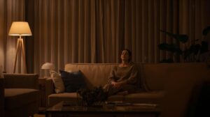 暖色の間接照明だけが灯る夜のリビングで、ソファに座って静かに目を閉じる女性